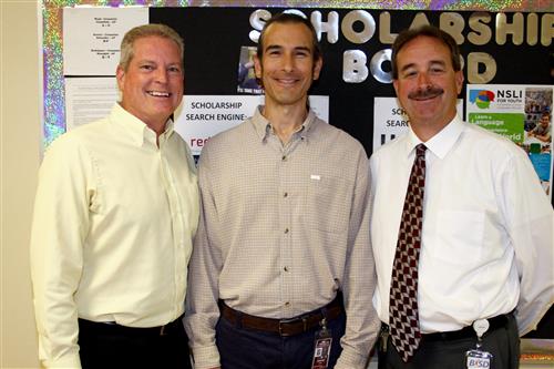 Photo of three men in front of bulletin board 